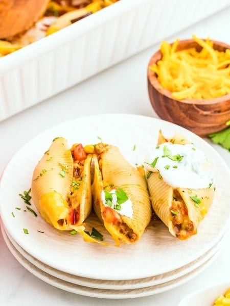 Three cheesy Taco Stuffed Shells on a white plate.