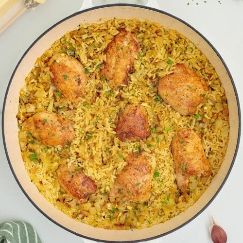 Topdown view of cooked Chicken Thighs and Rice in a white skillet.
