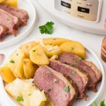A Corned Beef and Cabbage with boiled potatoes on a white plate.