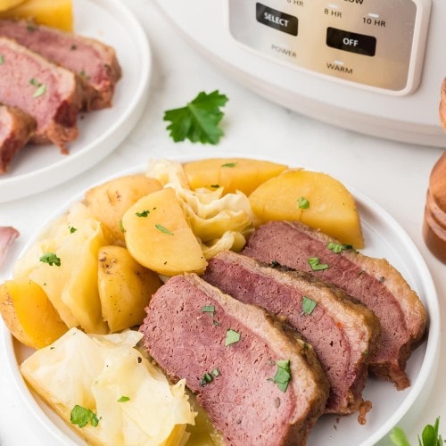 A Corned Beef and Cabbage with boiled potatoes on a white plate.