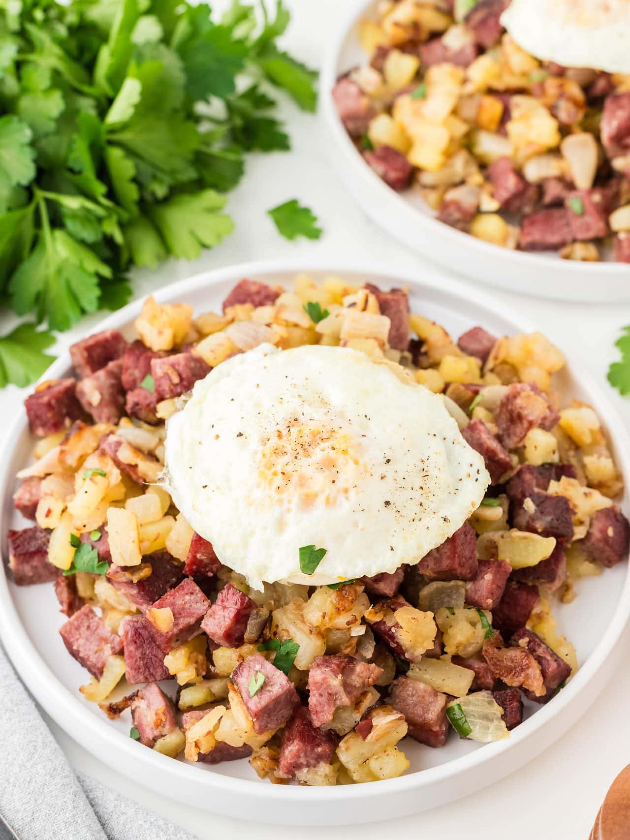 Top down view of Corned Beef Hash topped with an over easy egg on a white plate.