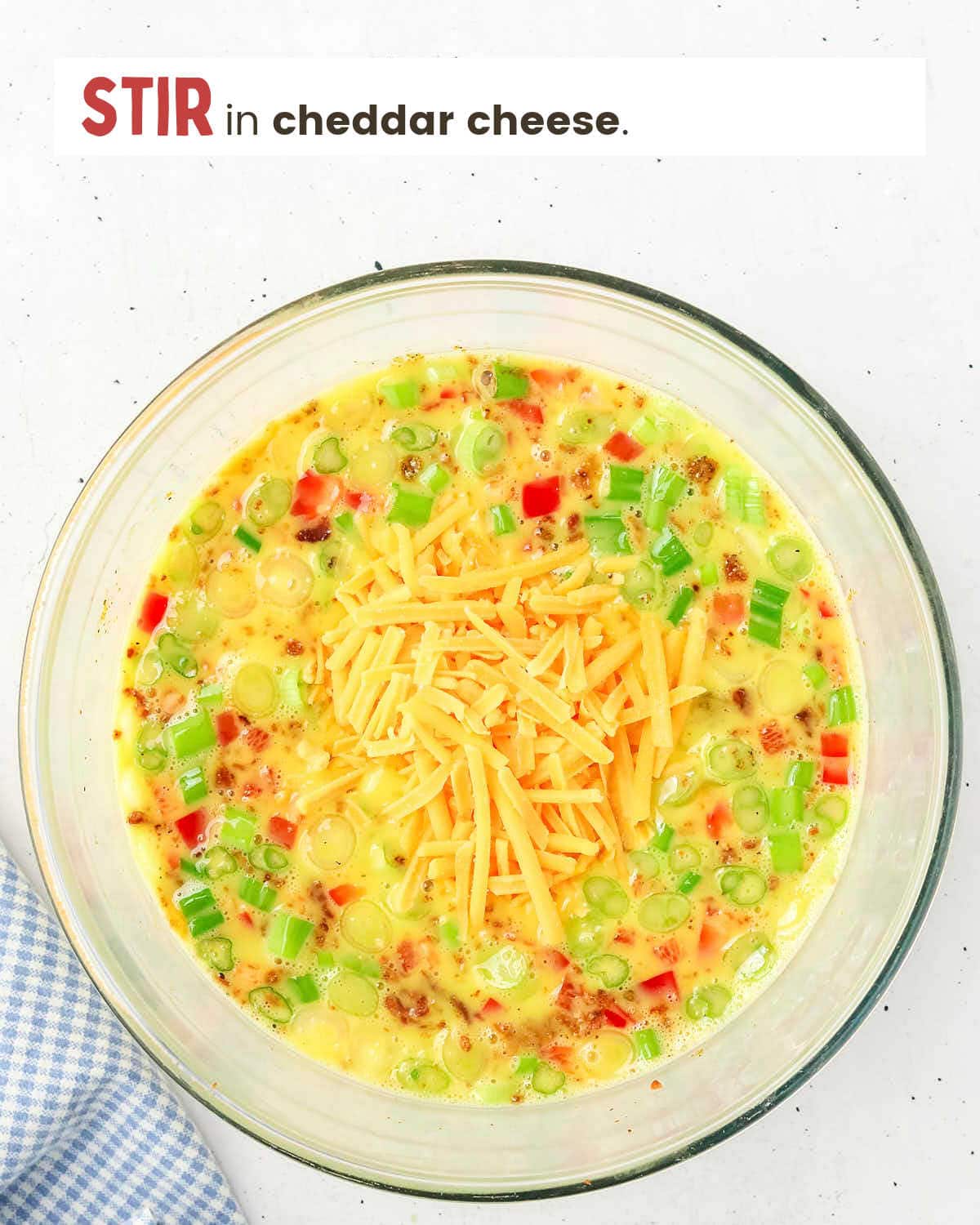Eggs mixed with milk, red peppers, green onions, and spices with shredded cheddar cheese on top.