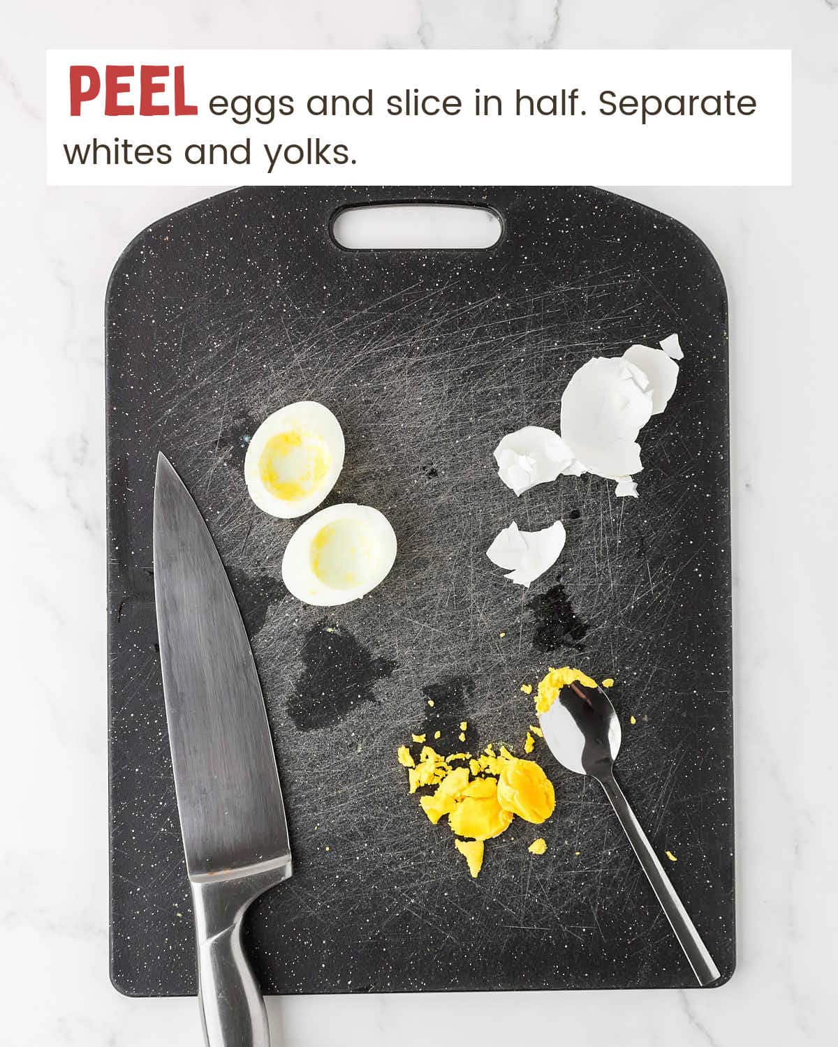 A black cutting board with a knife, sliced hard boiled egg white, egg shell pieces, egg yolk, and a fork.