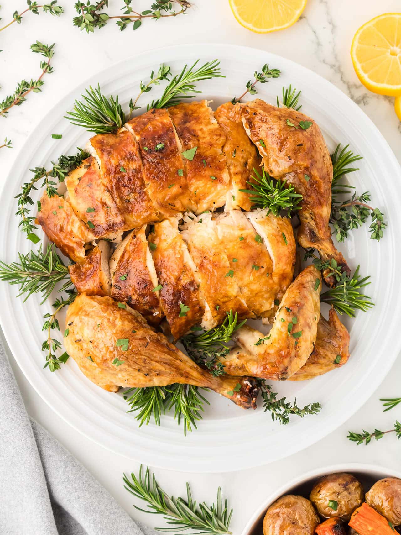 Carved Roasted Chicken on a white plate served with fresh herbs.