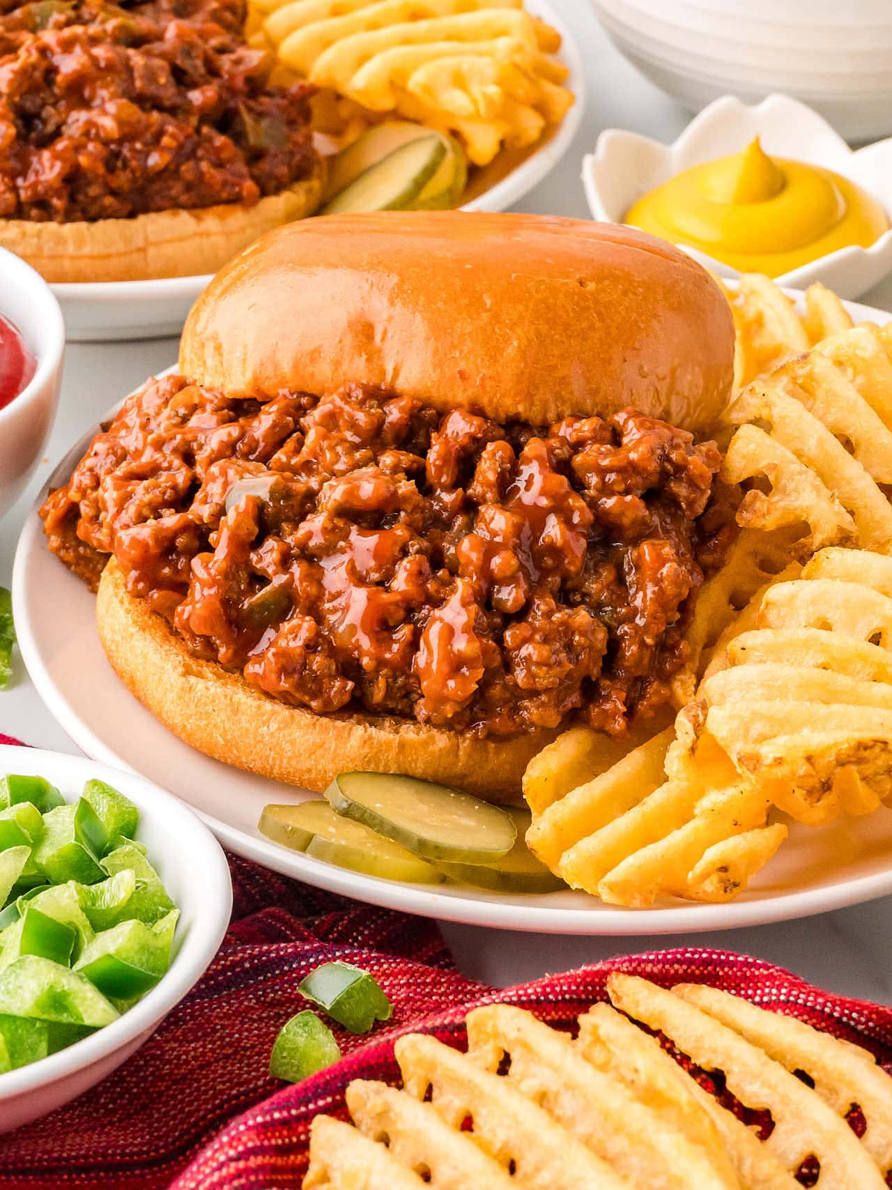 Closeup of a Sloppy Joes with waffle fries on a white plate.