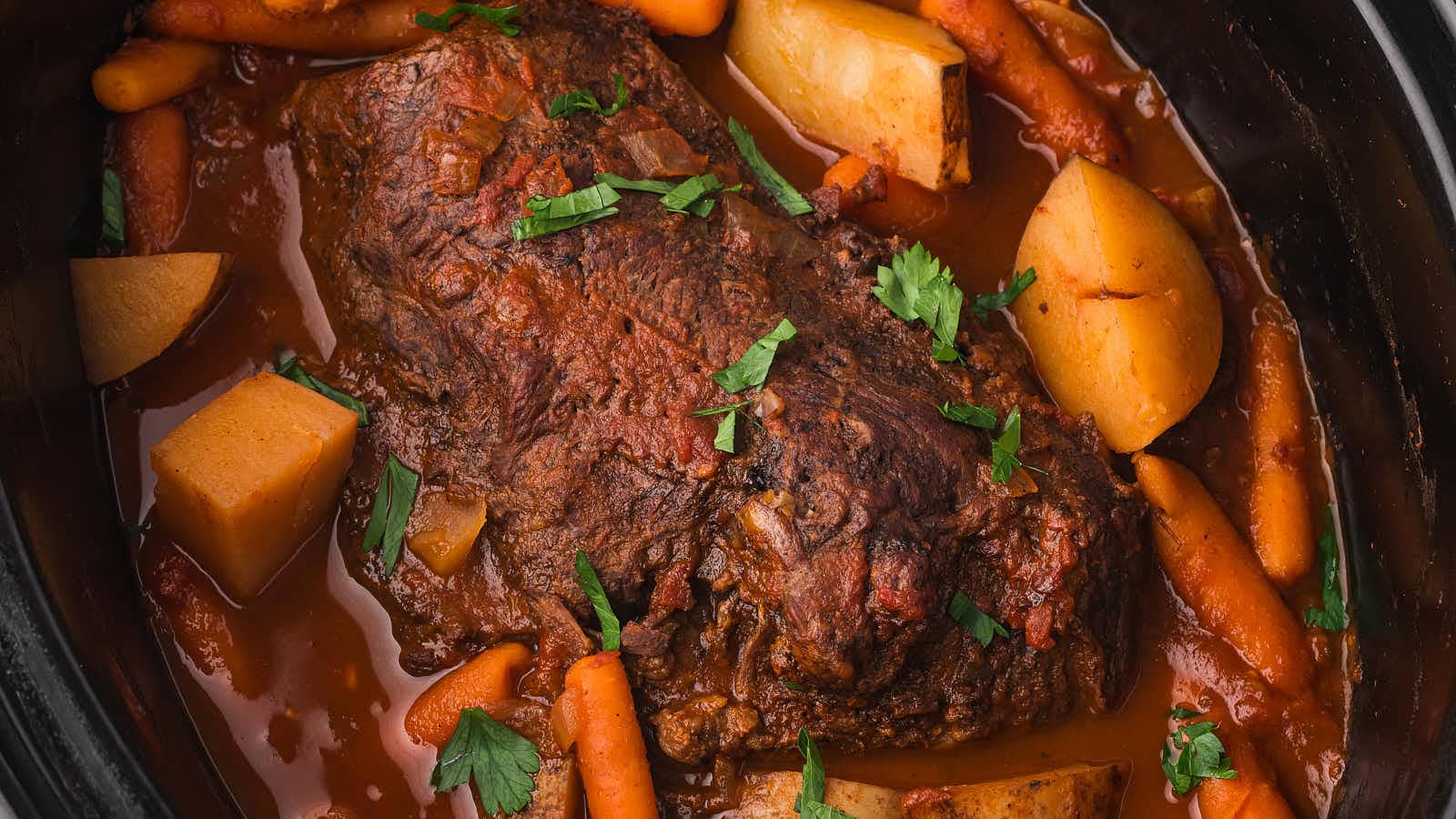Slow cooker pot roast with carrots, potatoes, and fresh parsley in a rich tomato sauce.