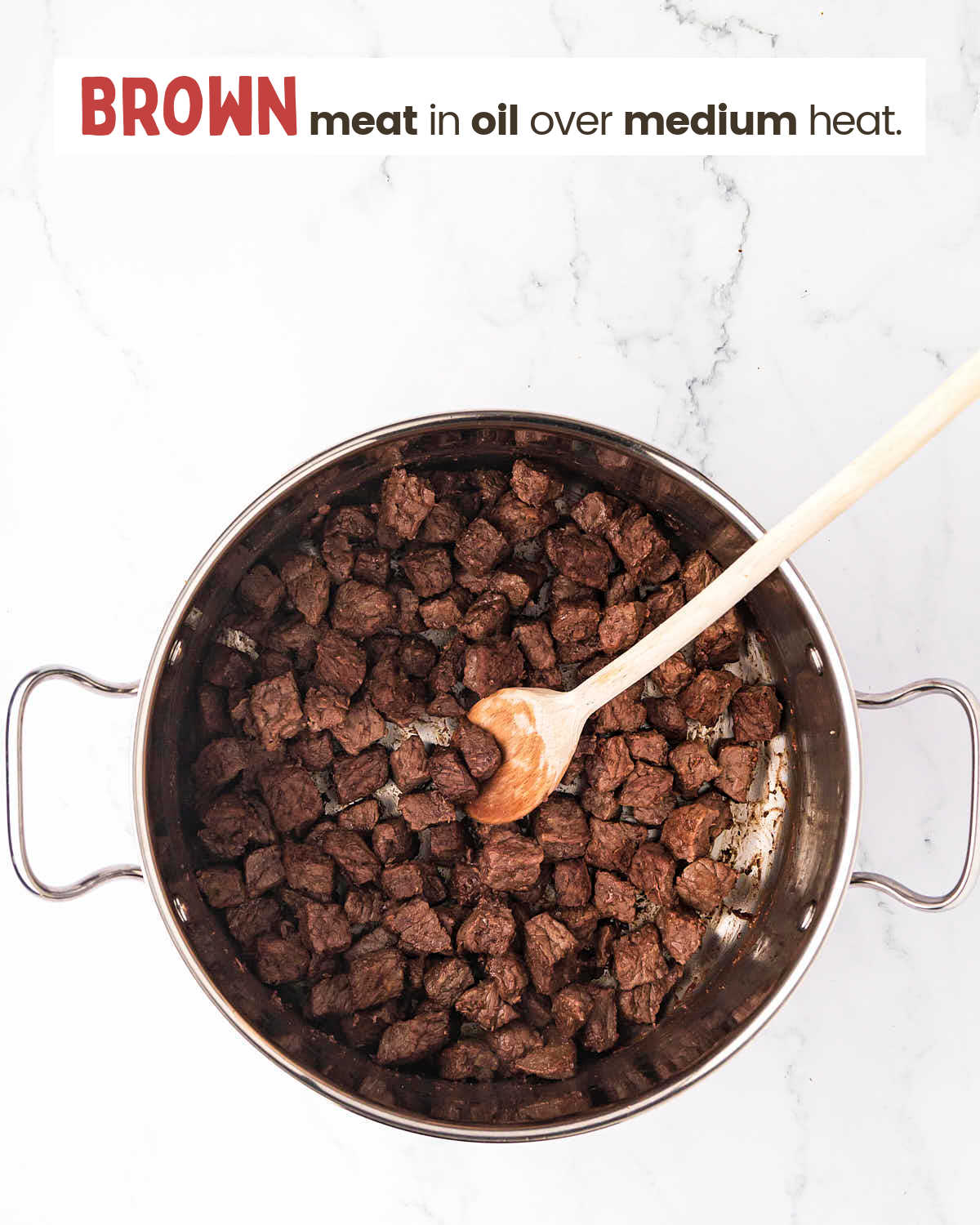 Browned steak pieces in a pot with a wooden spoon.