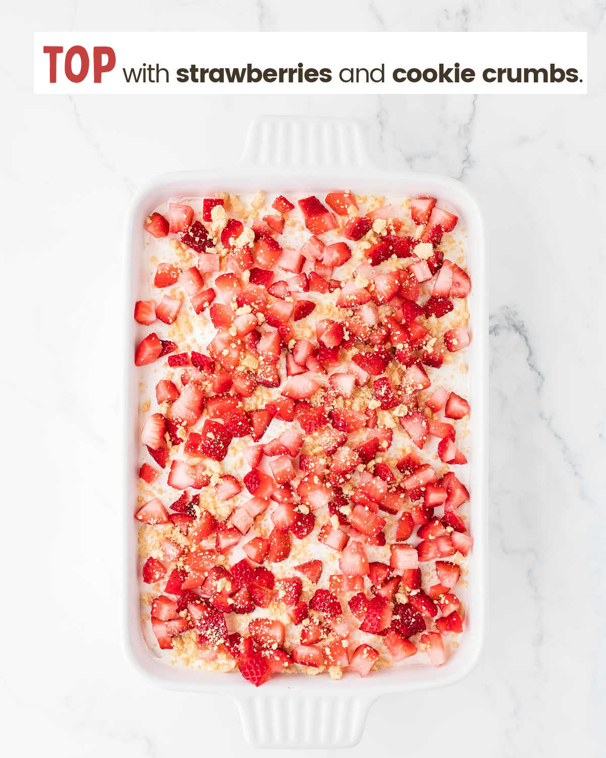 Strawberry delight dessert in a baking dish. It's topped with strawberry pieces and cookie crumbs.