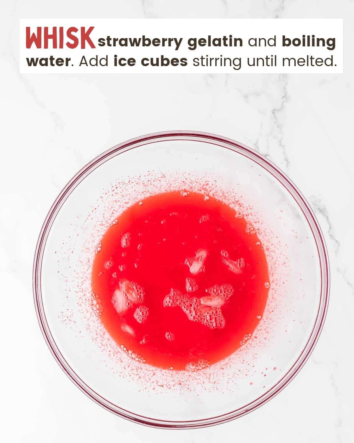 Strawberry gelatin mixed with water and ice cubes in a bowl.