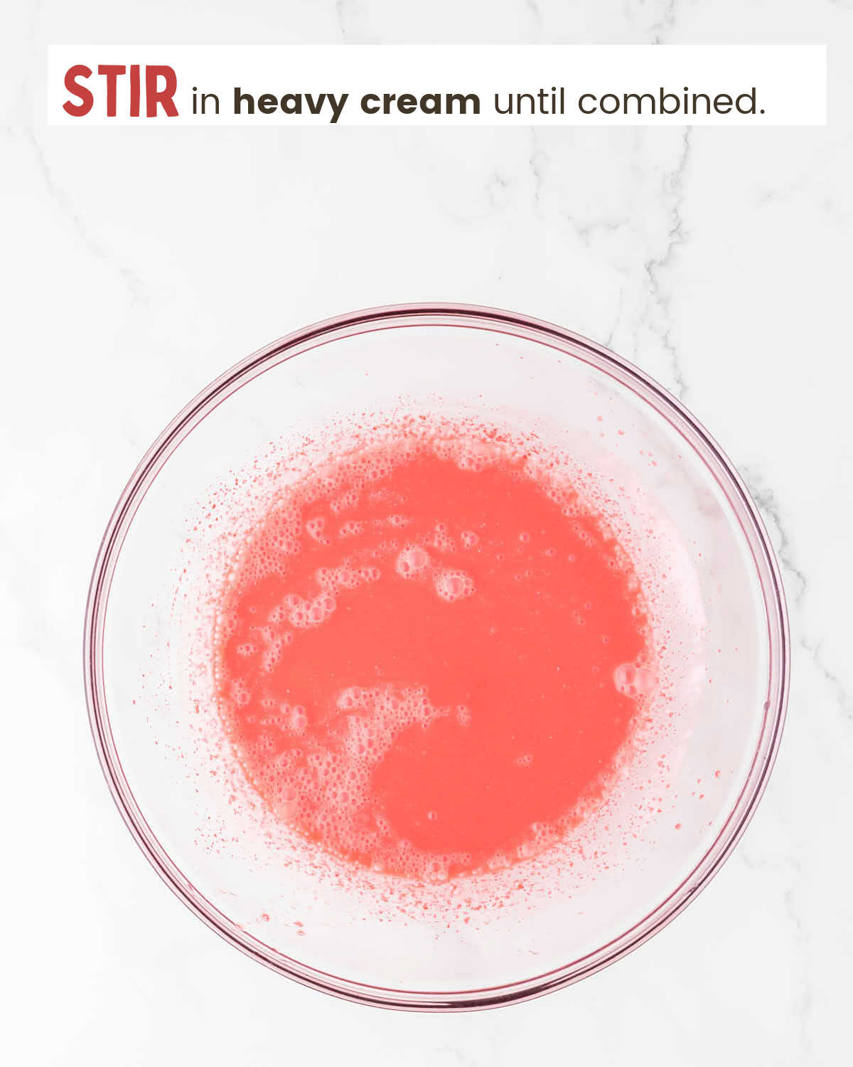 Strawberry gelatin mixture mixed with heavy cream in a bowl.