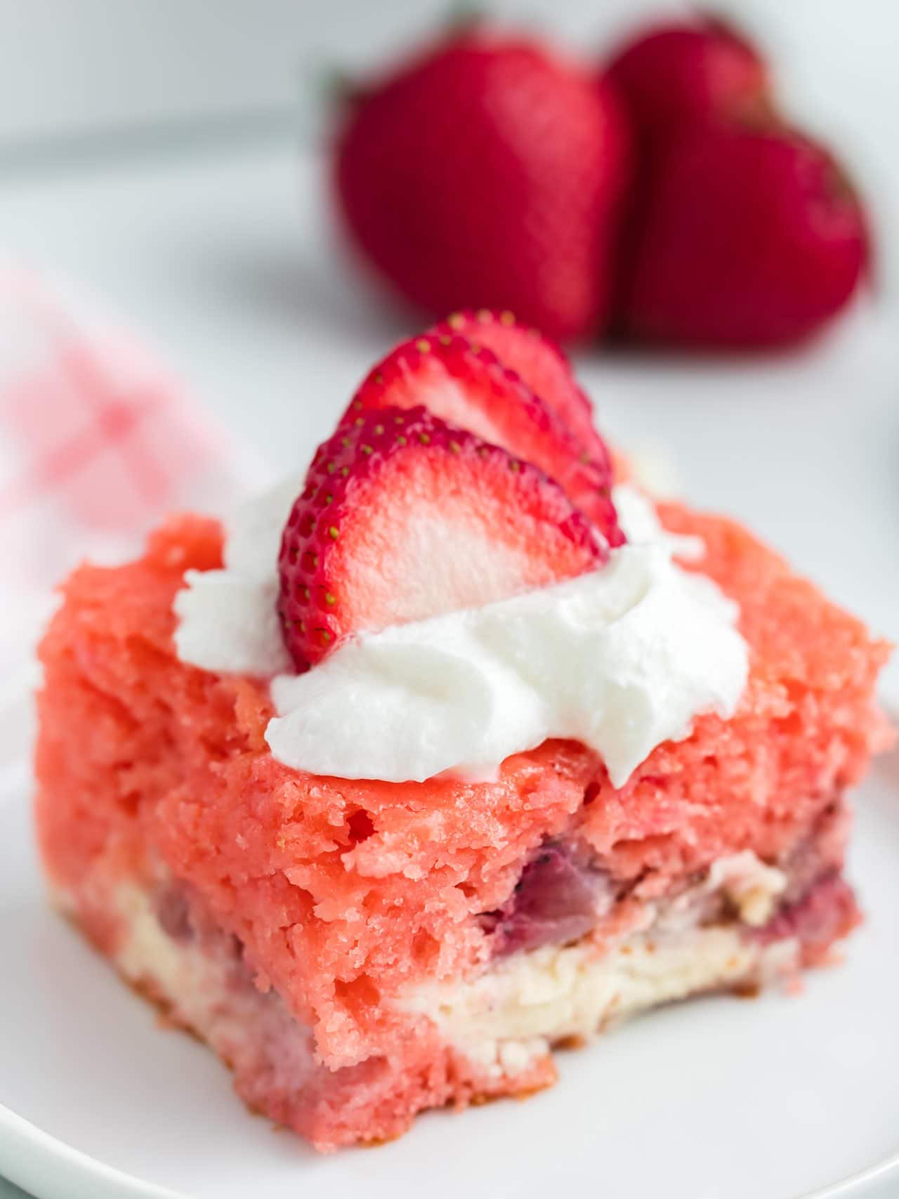 A slice of Strawberry Earthquake Cake topped with whipped cream and fresh strawberries.