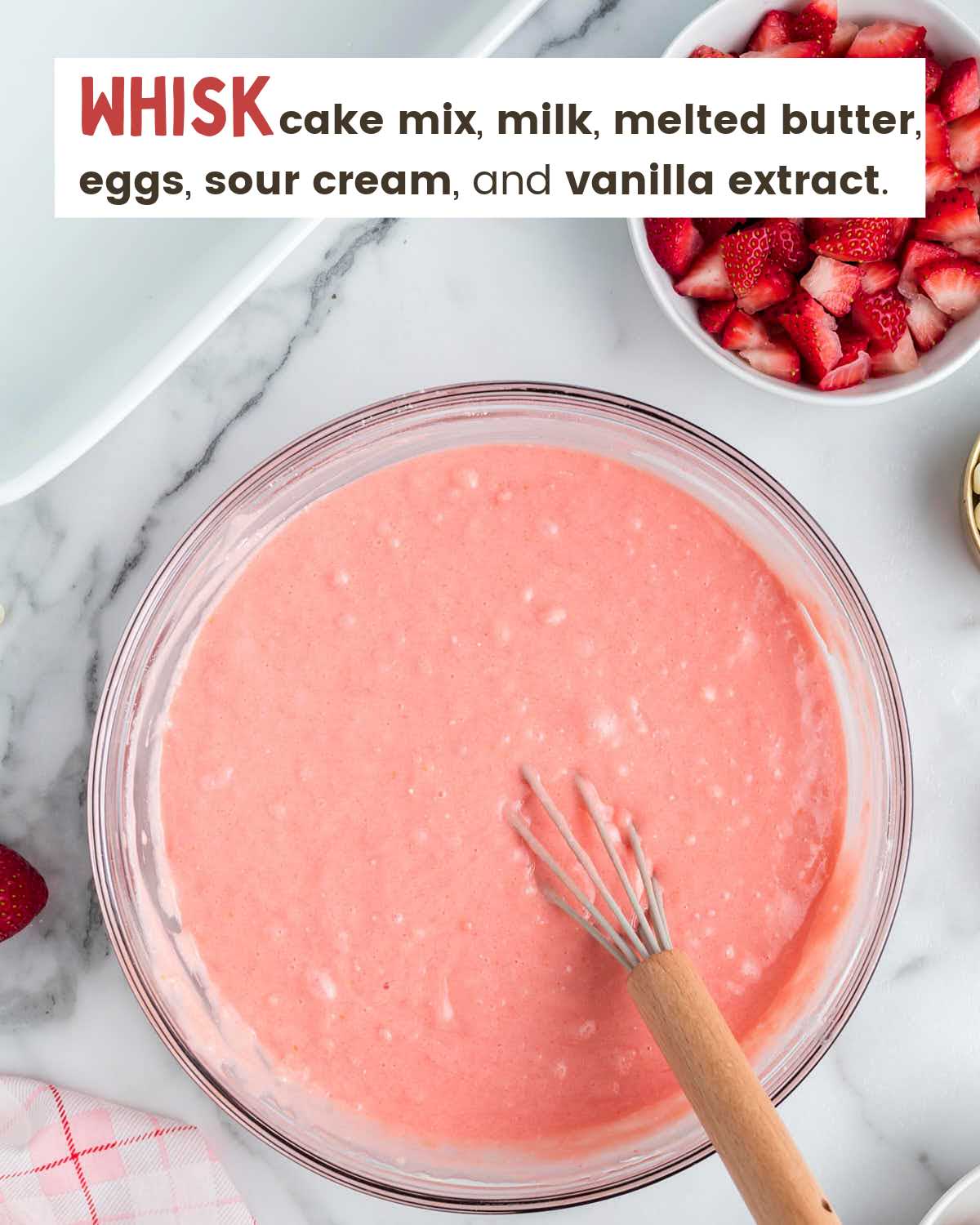 A whisk in a bowl filled with strawberry cake batter. 