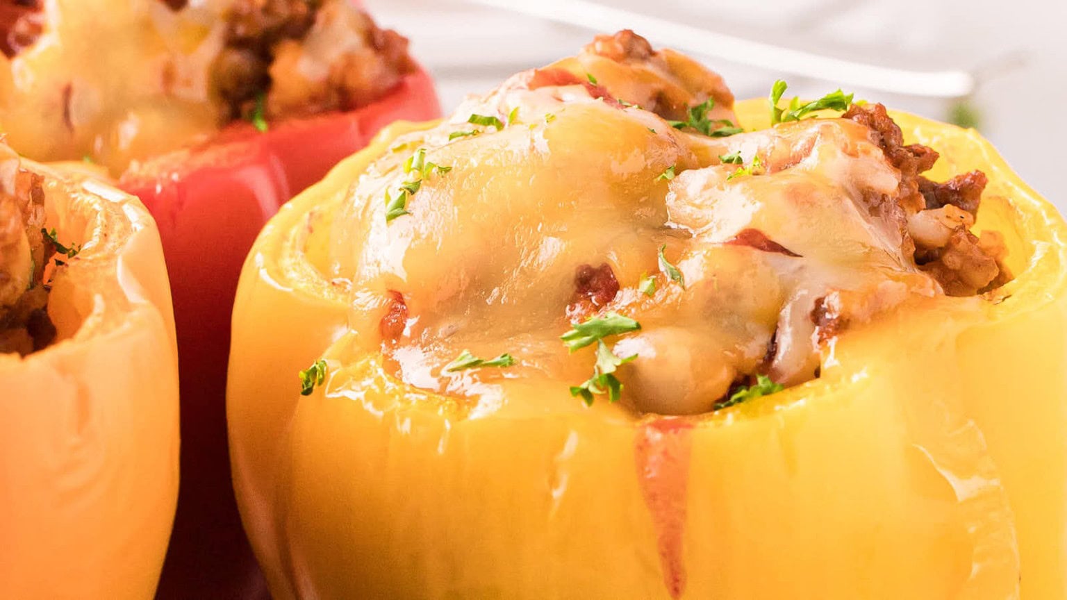 Colorful stuffed bell peppers filled with seasoned meat and topped with melted cheese and fresh parsley.