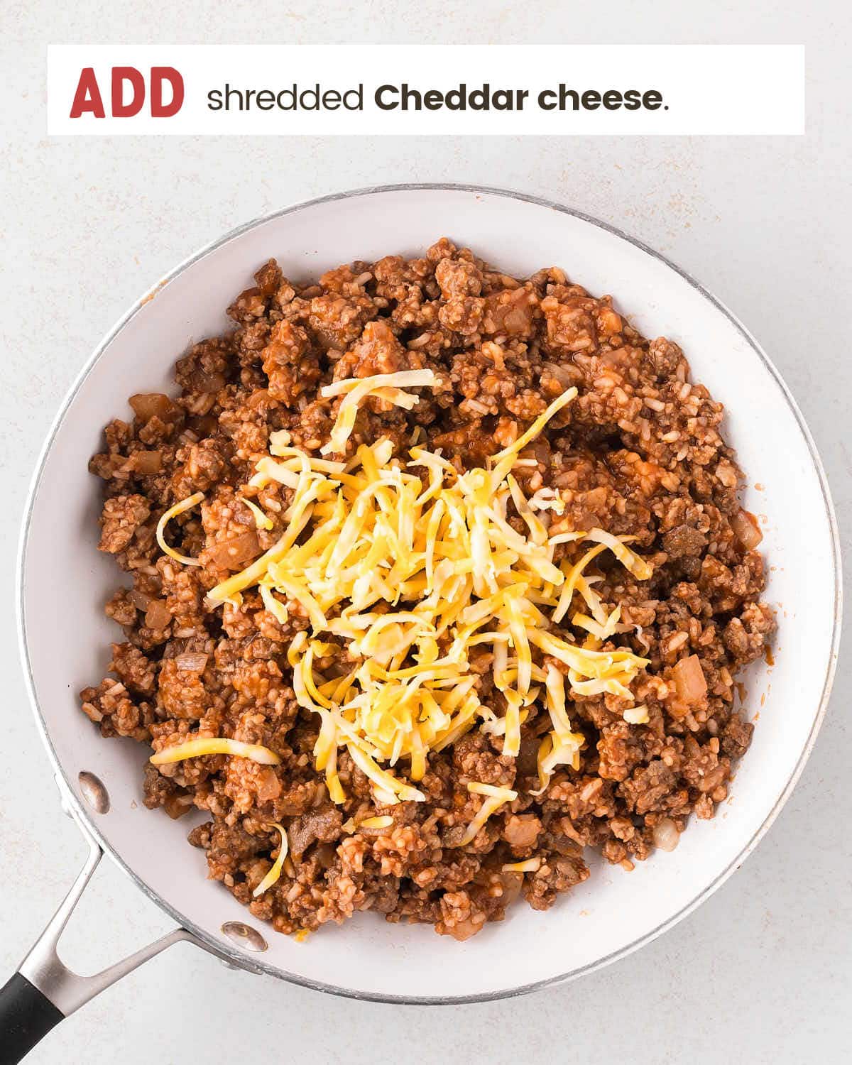 Cooked meat mixture with shredded cheese on top in a skillet.