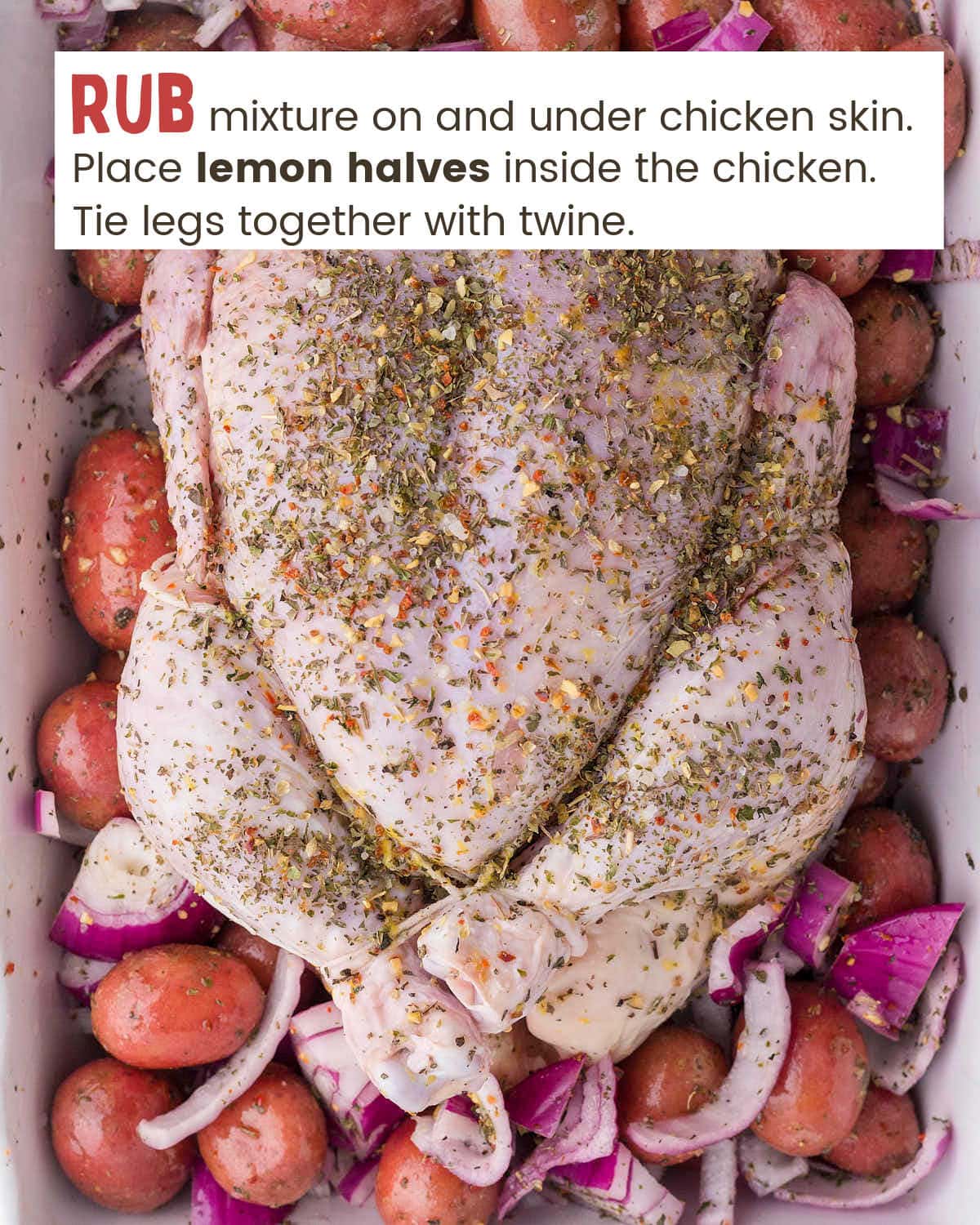 Raw whole chicken covered with seasoning in a baking dish with onions and potatoes.