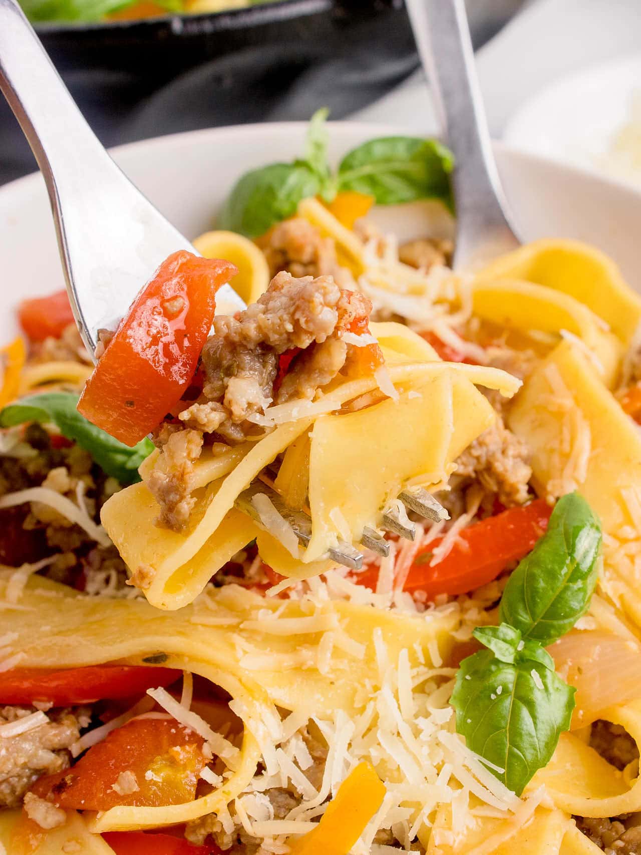 Two fork picking up Italian Drunken Noodles off a plate.