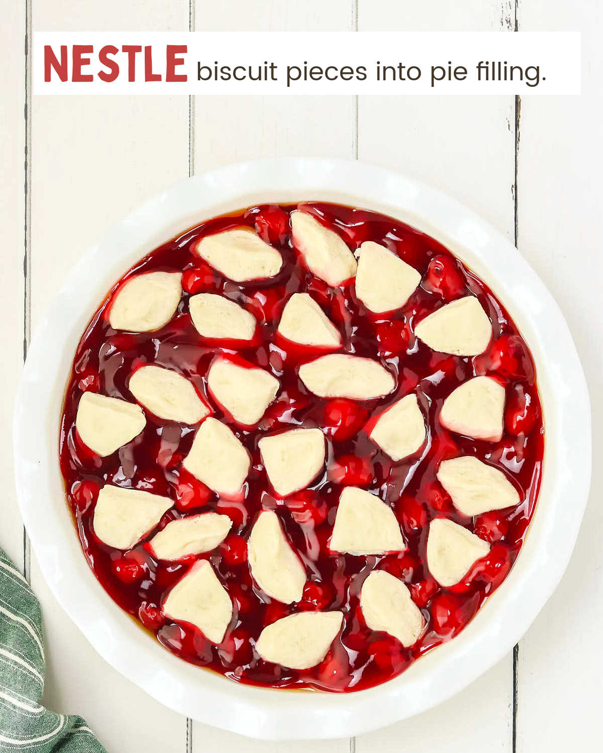 Cherry pie filling topped with biscuit pieces in a white pie plate.