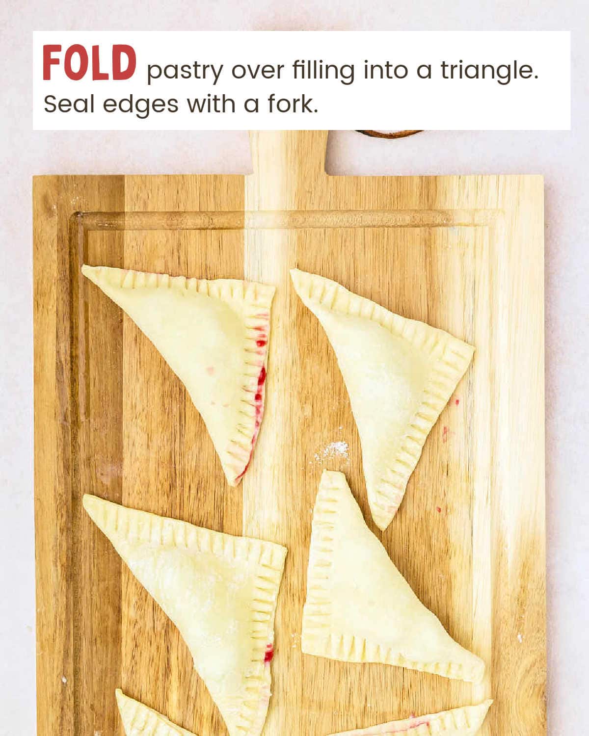 Puff pastry triangles filled with cherry mixture on a cutting board.