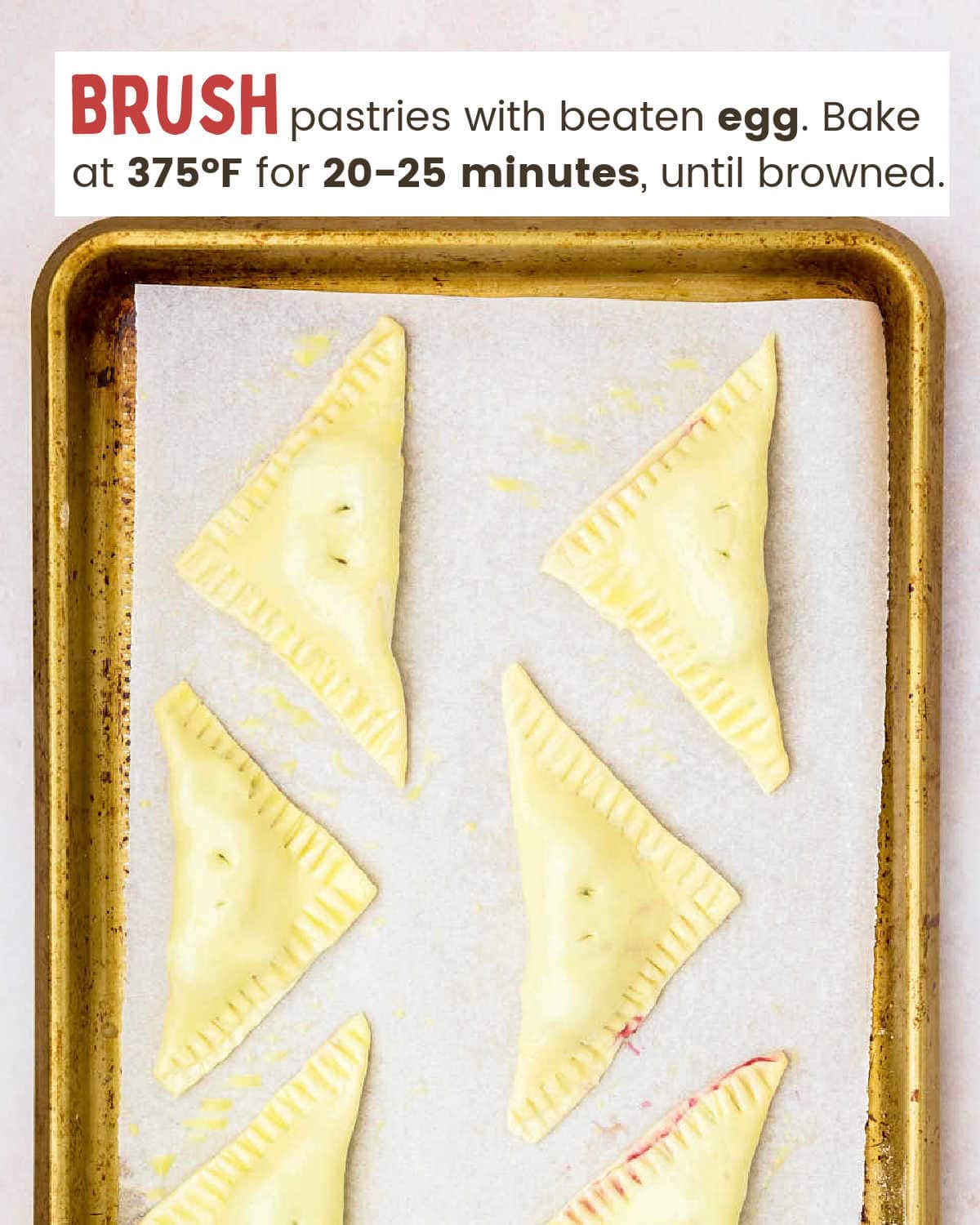 Puff pastry triangles filled with cherry mixture on a baking sheet lined with parchment paper.