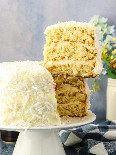 Lifting a slice of Coconut Cake with a cake lifter off a plate.