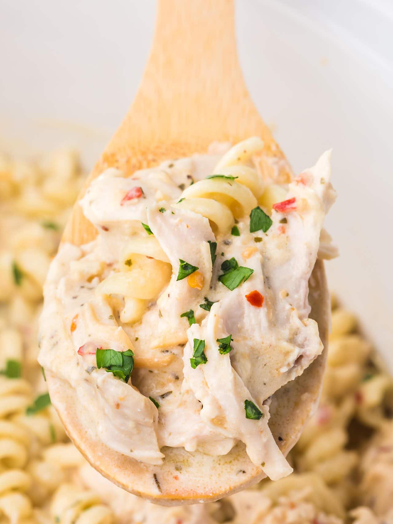 A wooden spoon full of Garlic Chicken Parmesan Pasta in a Crock Pot. 