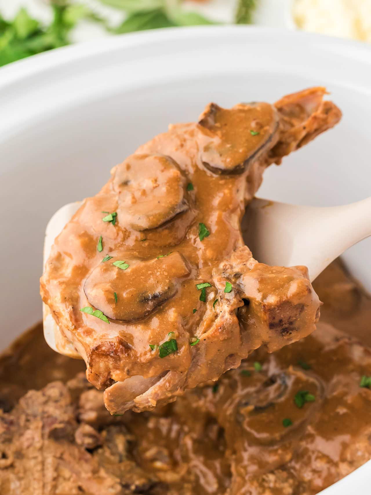 A cooked pork chop being removed from a Crock Pot.