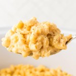 A large serving spoon of cheesy Mac and Cheese made in a Crockpot.