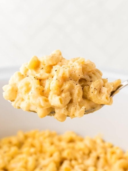 A large serving spoon of cheesy Mac and Cheese made in a Crockpot.