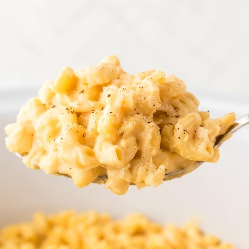 A large serving spoon of cheesy Mac and Cheese made in a Crockpot.