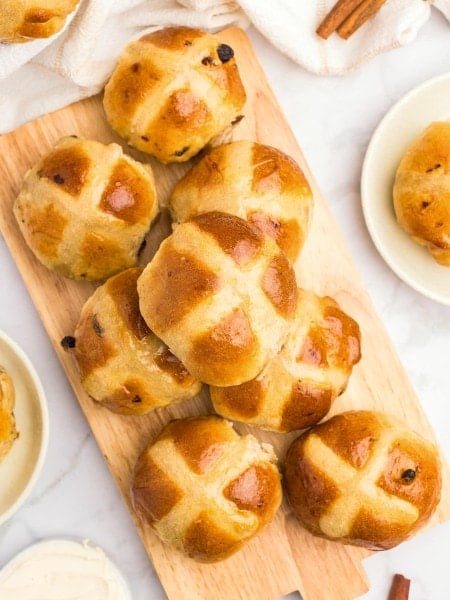 Freshly baked Hot Cross Buns on a wooden plate.