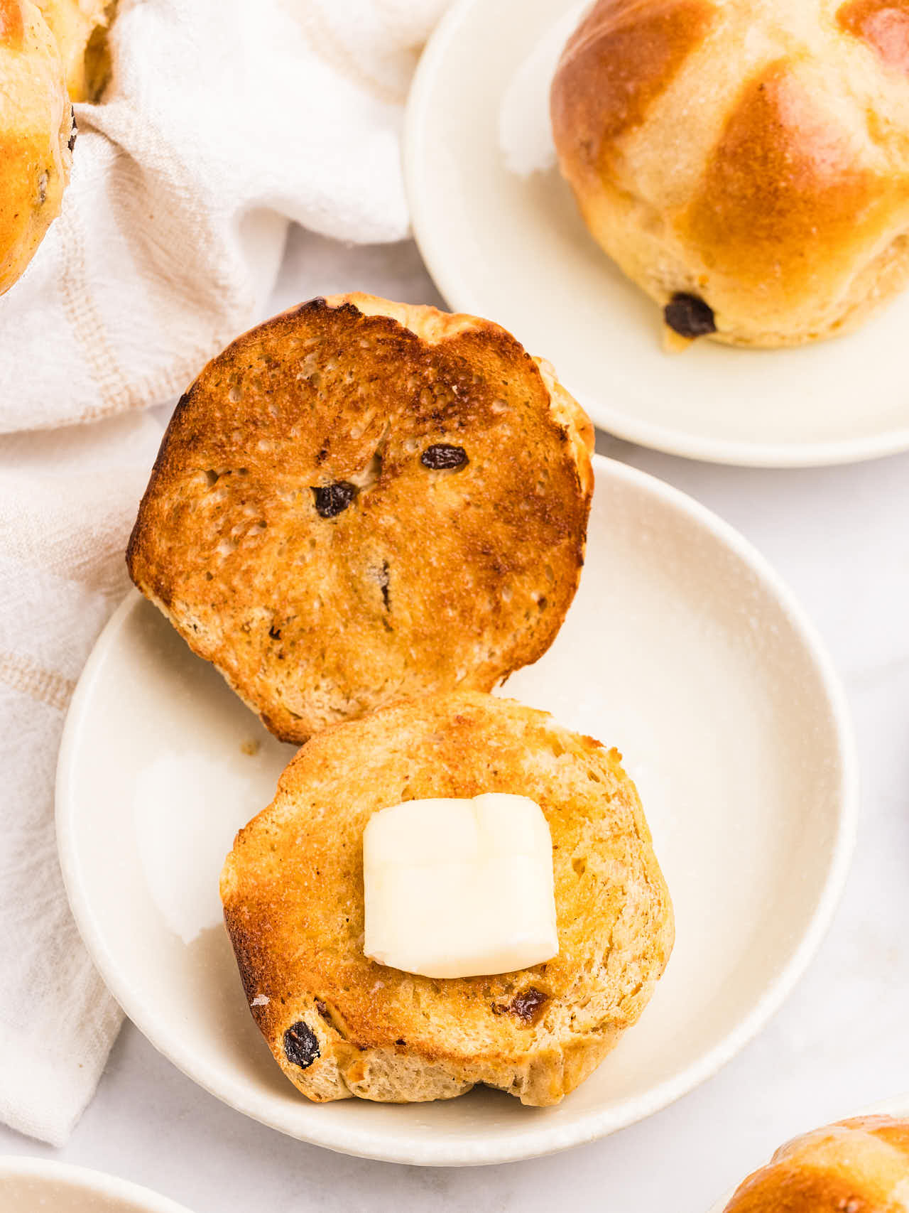 An open faced toasted Hot Cross Bun with a slice of butter.