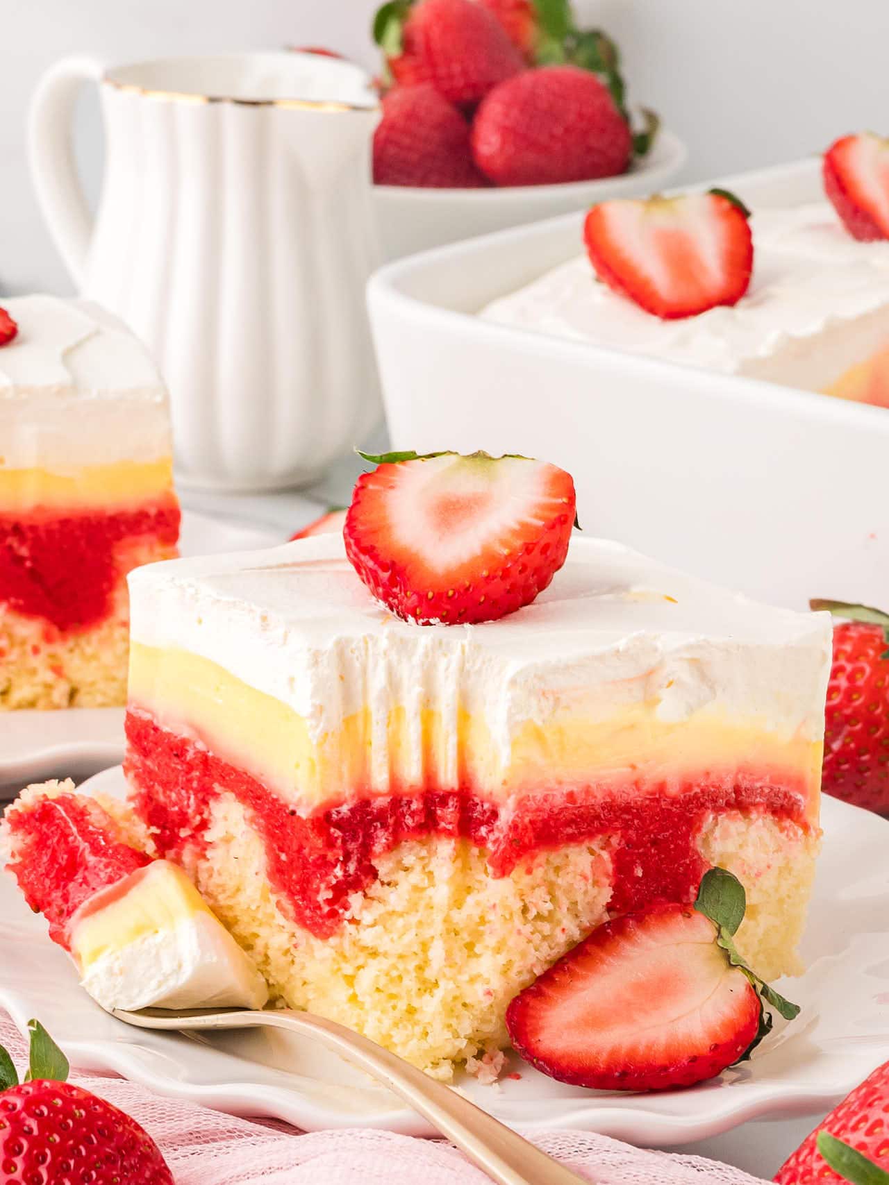 A slice of Strawberry Poke Cake on a white plate with a forkful of cake.