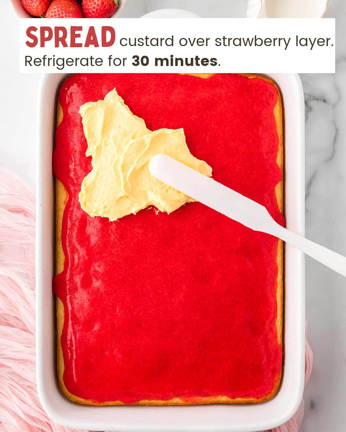 Custard being spread over strawberry layer of a cake with a spatula.