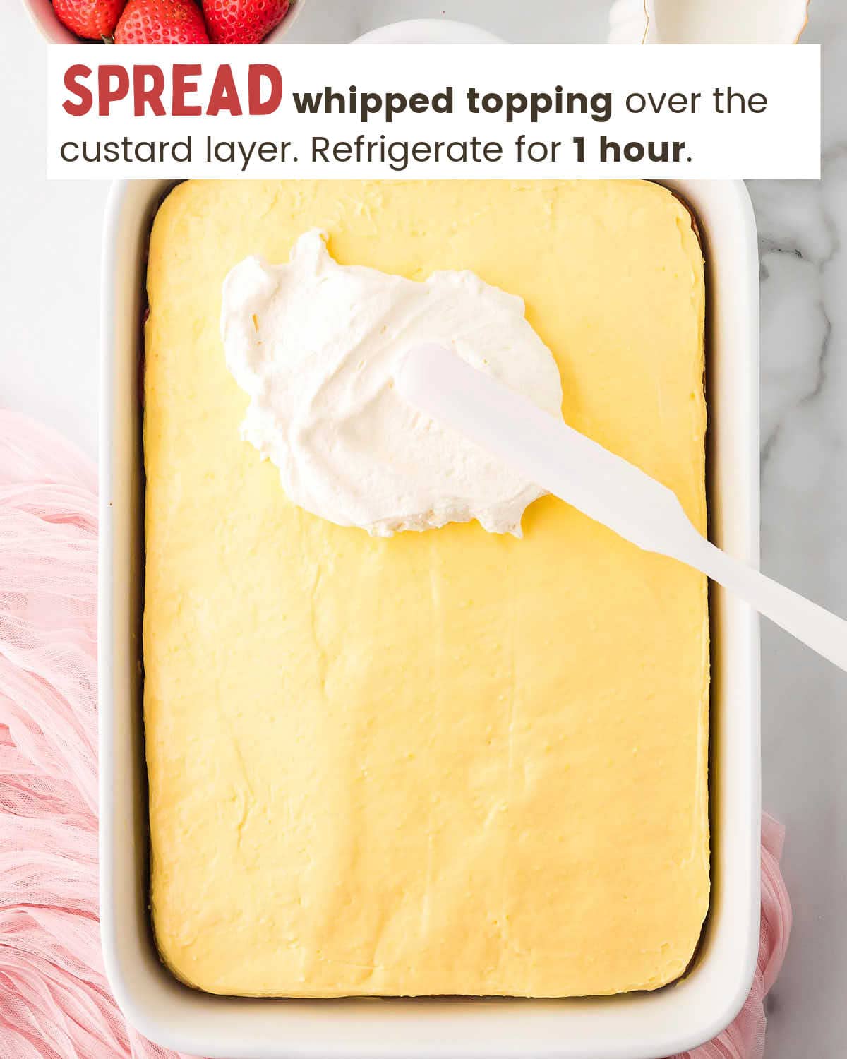 Whipped topping being spread over custard layer of a cake with a spatula.