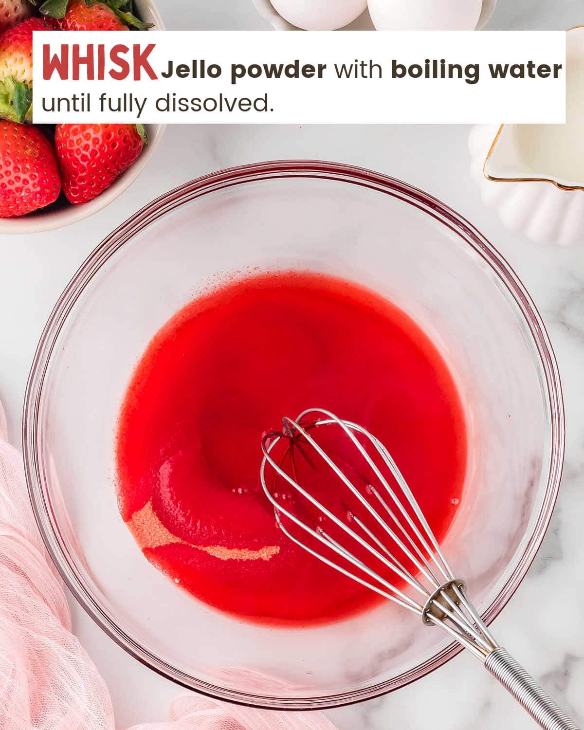 Strawberry Jello powder being whisked with boiling water in a mixing bowl.