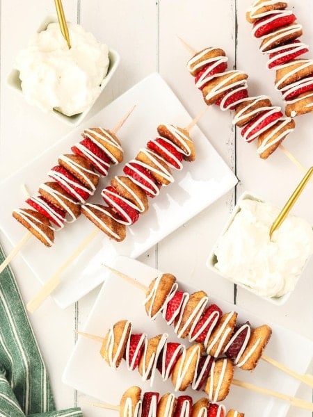 Strawberry Shortcake Kebobs drizzled with white chocolate on plate with whipped cream.