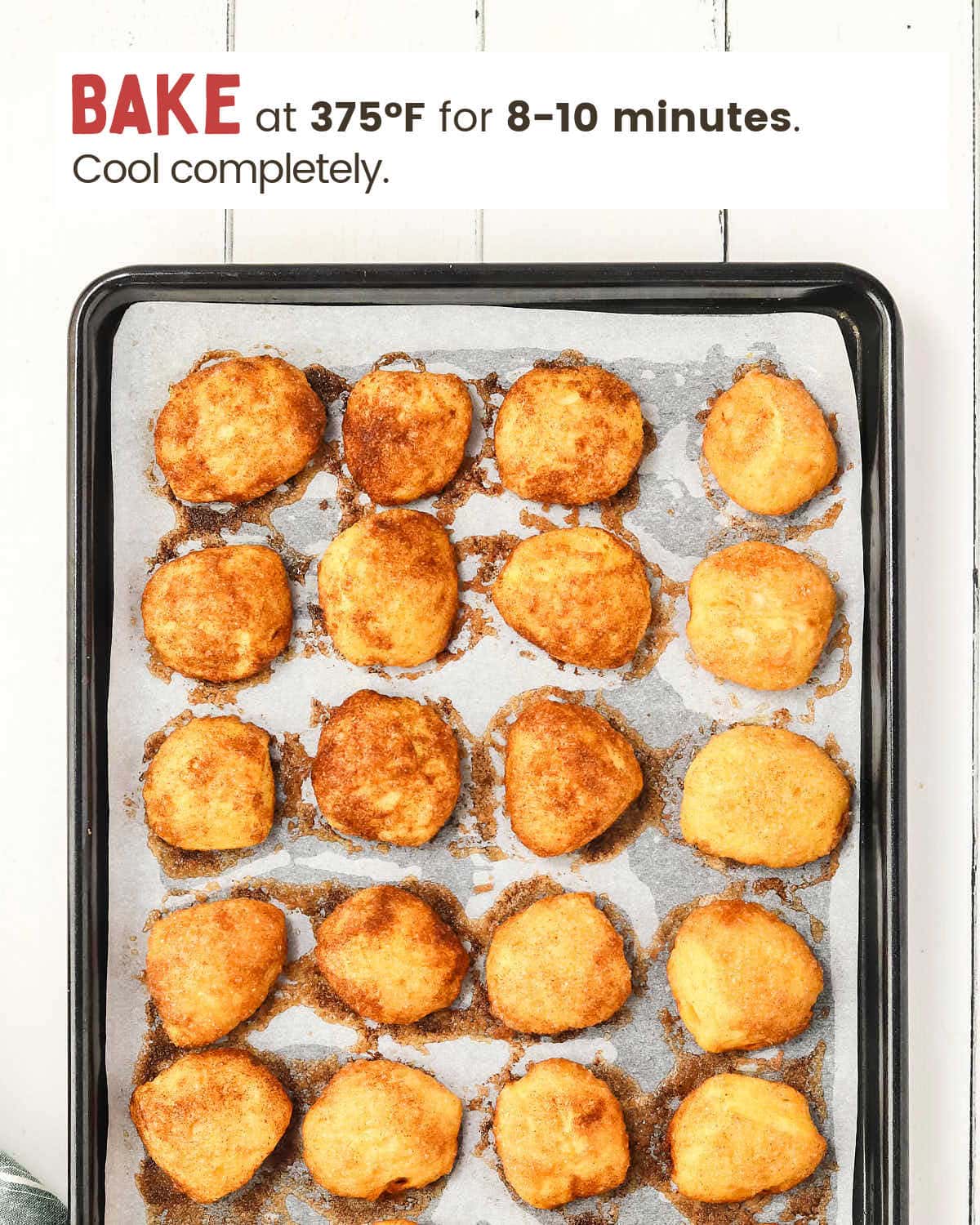 Baked biscuit discs coated with cinnamon and sugar on a parchment-paper-lined baking sheet.