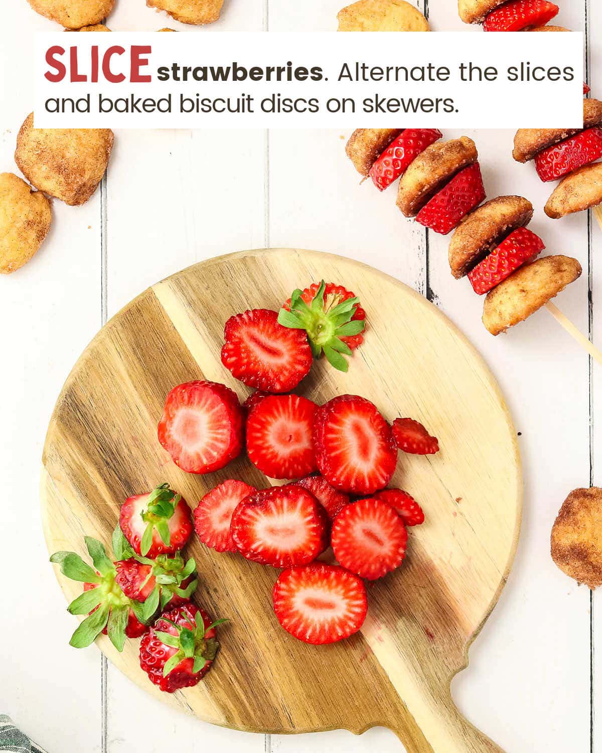 Sliced strawberries on a cutting board next to a skewer with sliced strawberries and biscuits.
