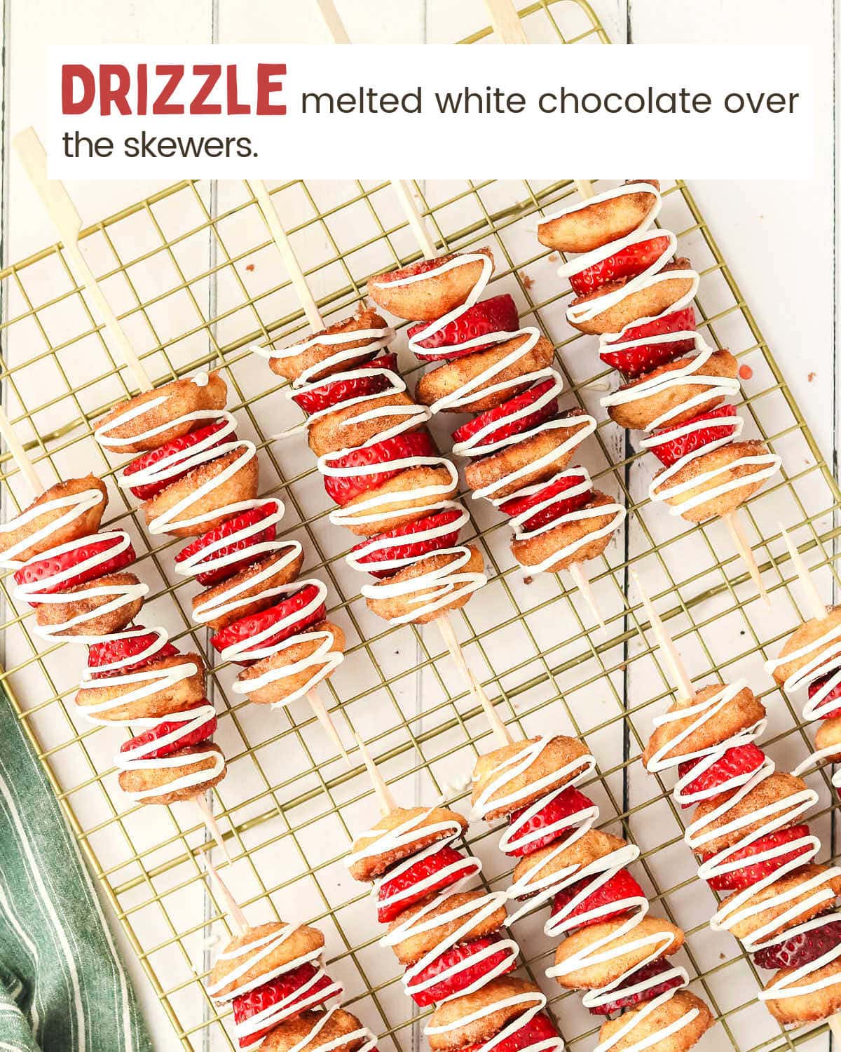 Strawberry shortcake kabobs drizzled with white chocolate on a cooling rack.