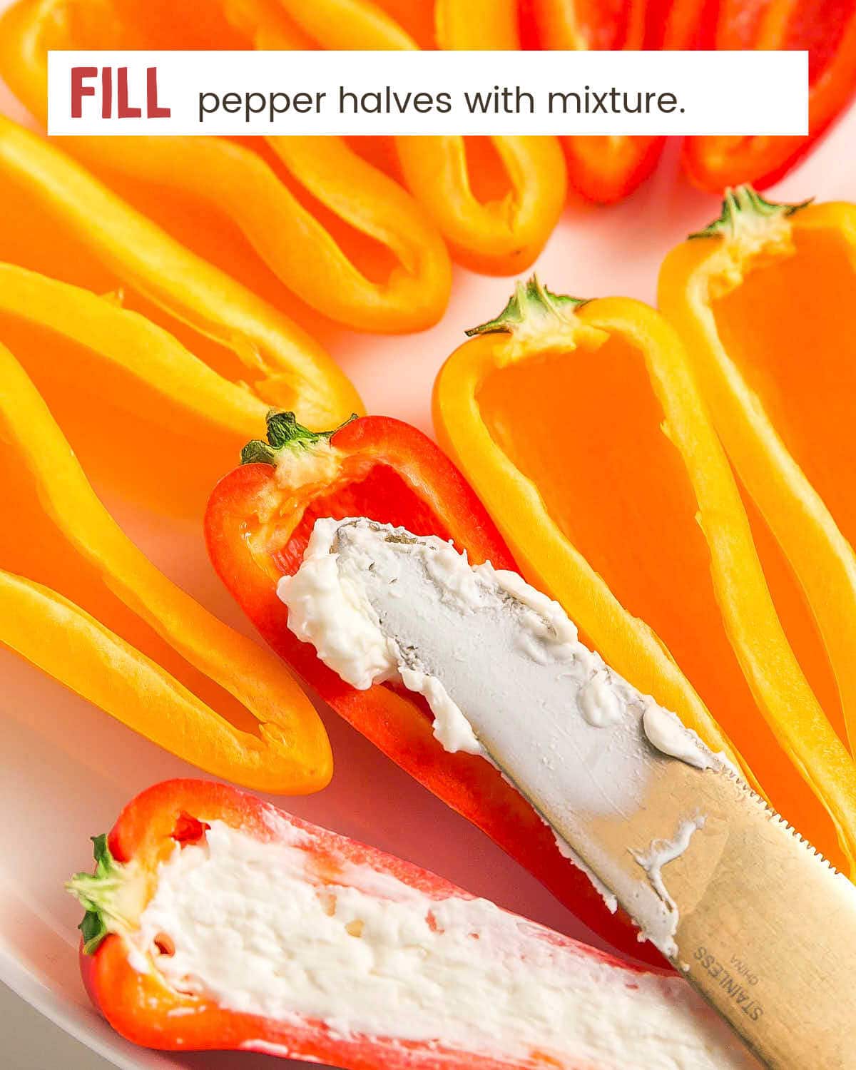 A knife spreading cheese mixture into a pepper half, next to a pepper that's already been filled.