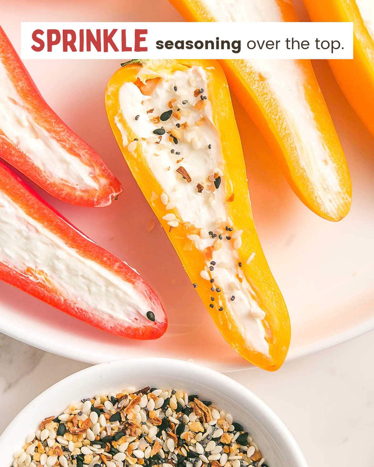 Stuffed mini peppers with one topped with everything bagel seasoning on a plate with a bowl of the seasoning nearby.