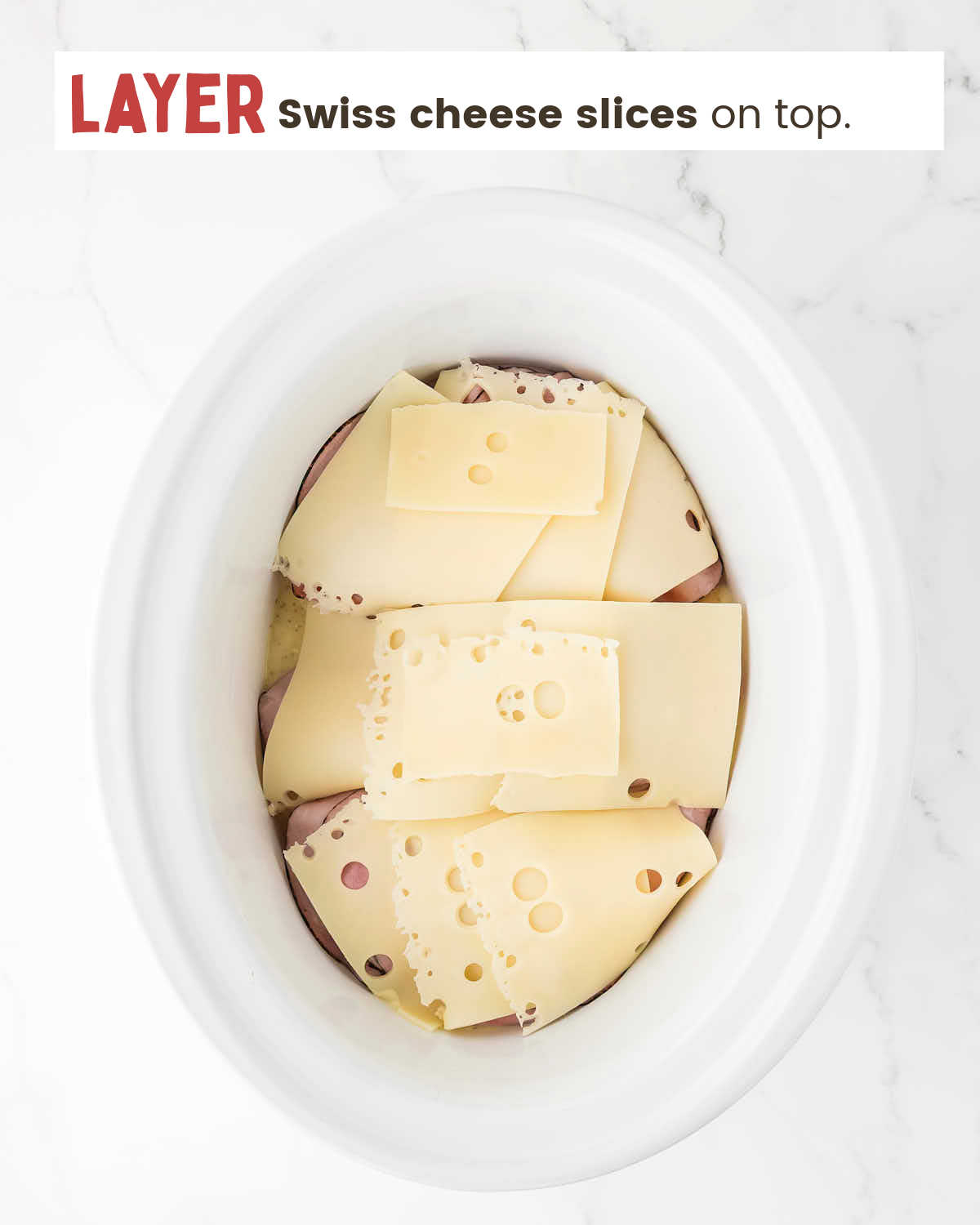 Swiss cheese slices over ham slices in a slow cooker.