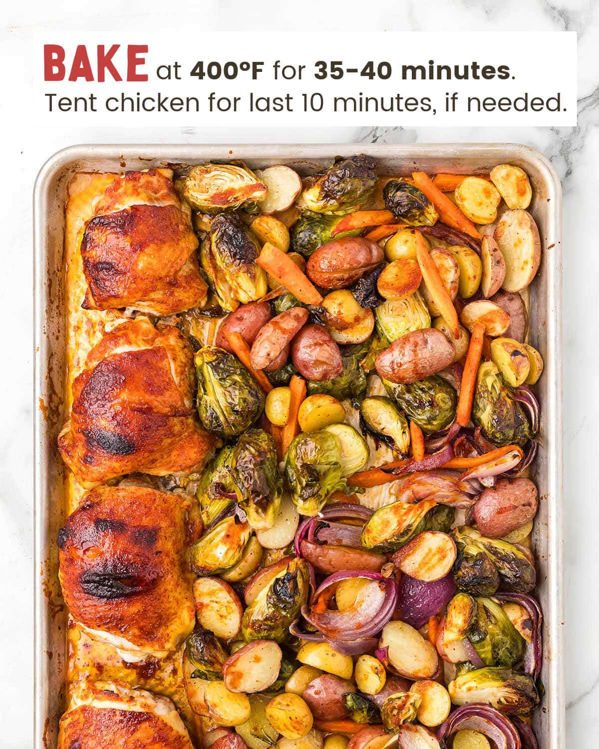 Baked Red onions, baby potatoes, sliced carrots, and Brussels sprouts next to honey siracha chicken thighs on a baking sheet.