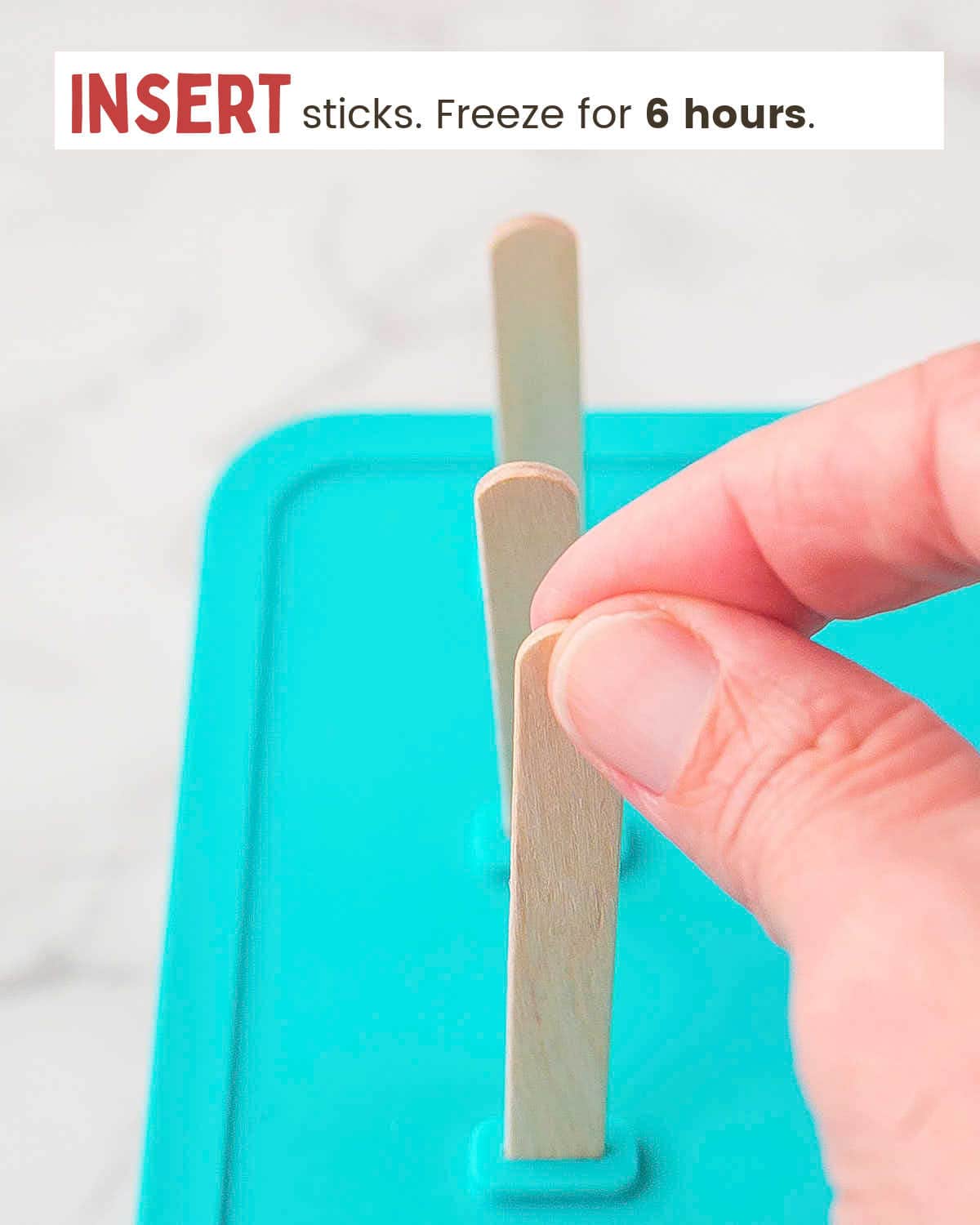 A hand places sticks into a popsicle mold.