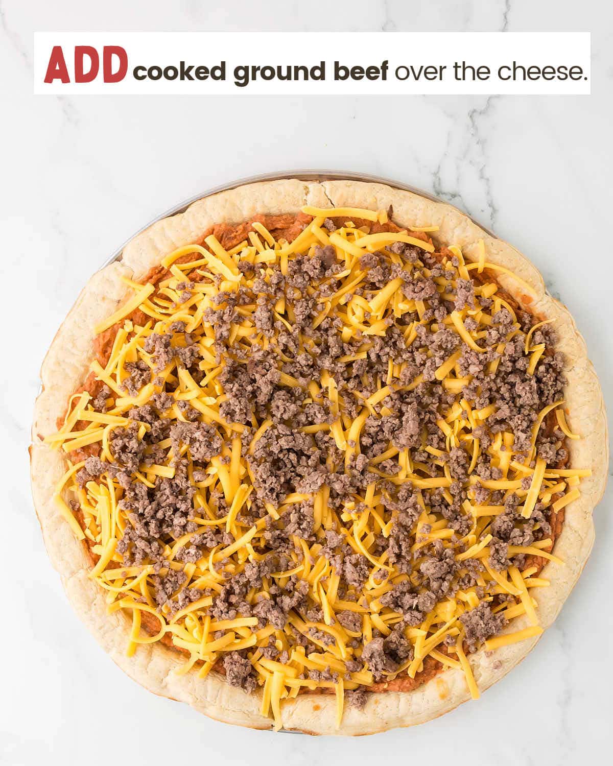 Refried bean mixture spread over pizza crust topped with cheese and cooked ground beef.