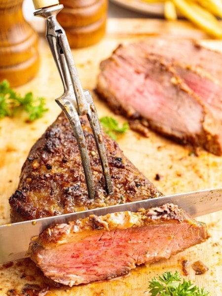 Slicing juicy oven-roasted Tri Tip Steak with a seared crust on a wooden cutting board.