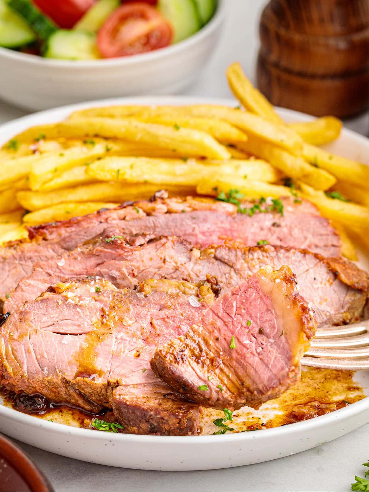 Sliced Tri Tip Steak served with French fries on a white plate.