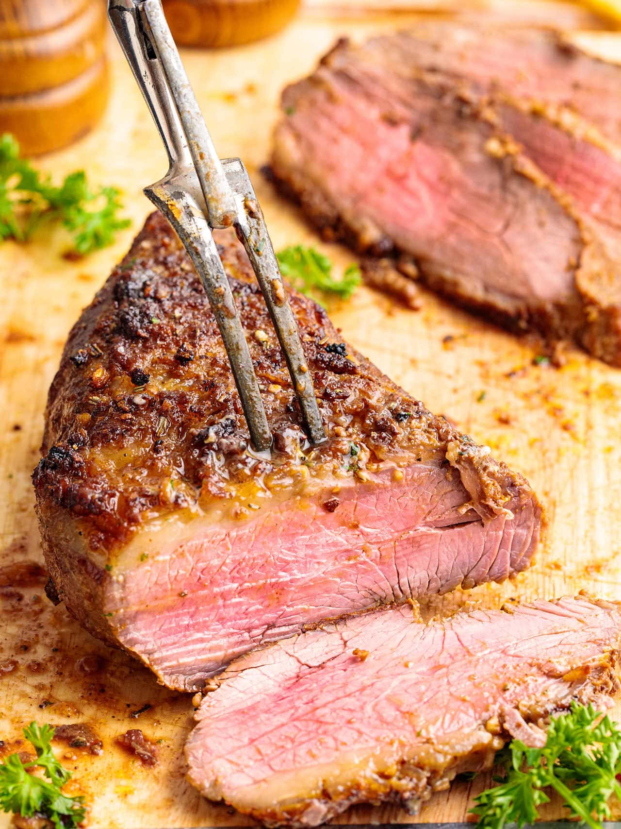 Medium-rare Tri Tip Steak sliced on a cutting board with seared crust and carving fork.