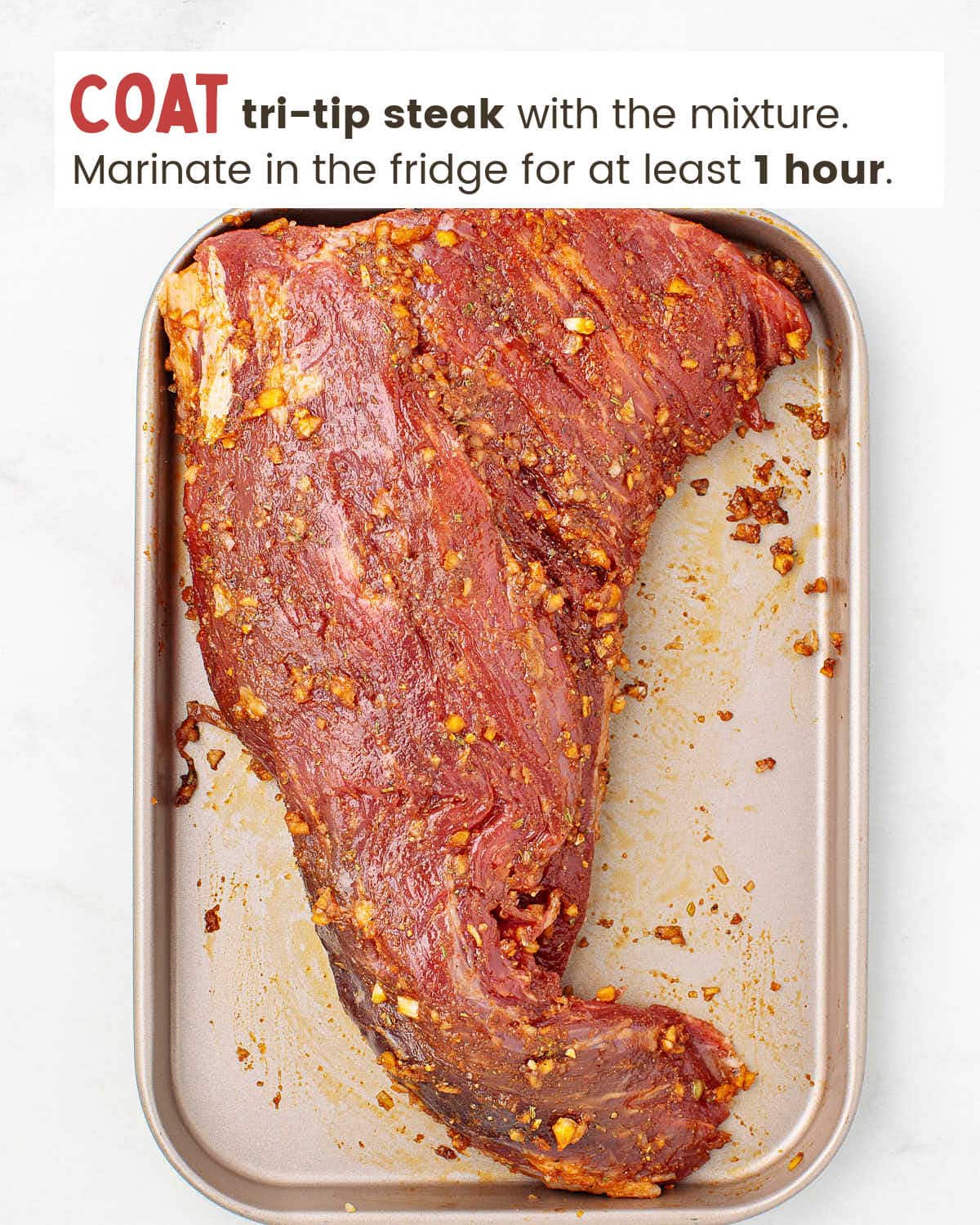 Tri-tip steak covered with a marinade on a baking sheet.