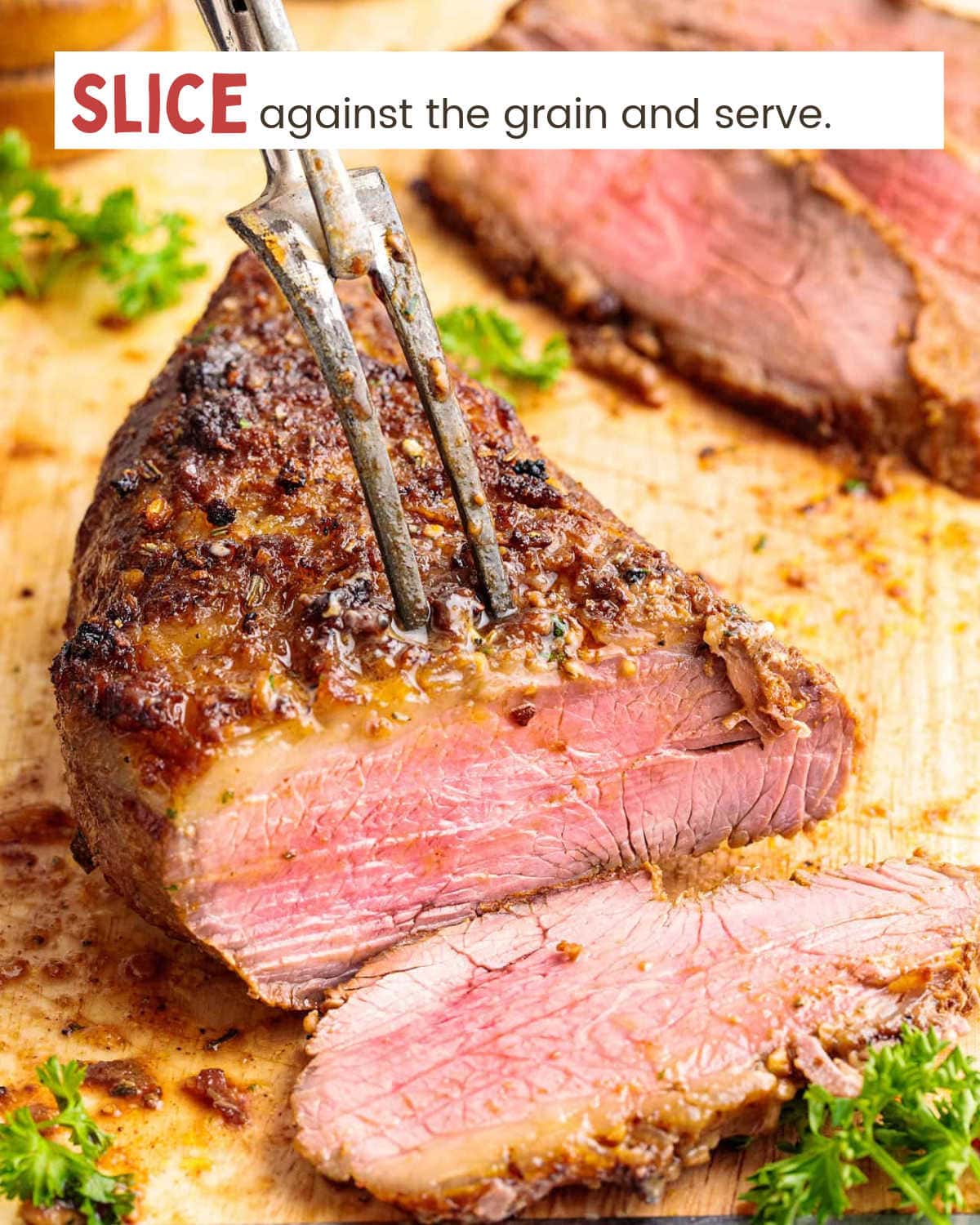 A large fork piercing a tri-tip steak that has just been sliced, with the slice in front of it.